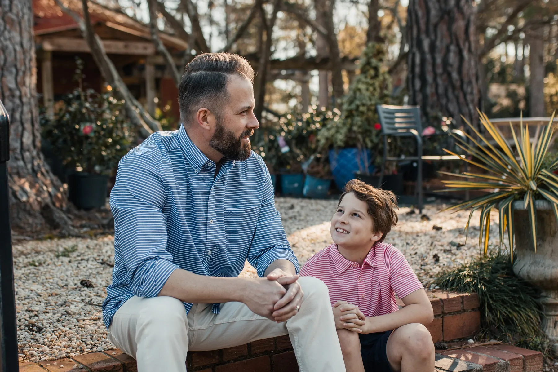 A father and his young son sitting outdoors together, both in striped shirts